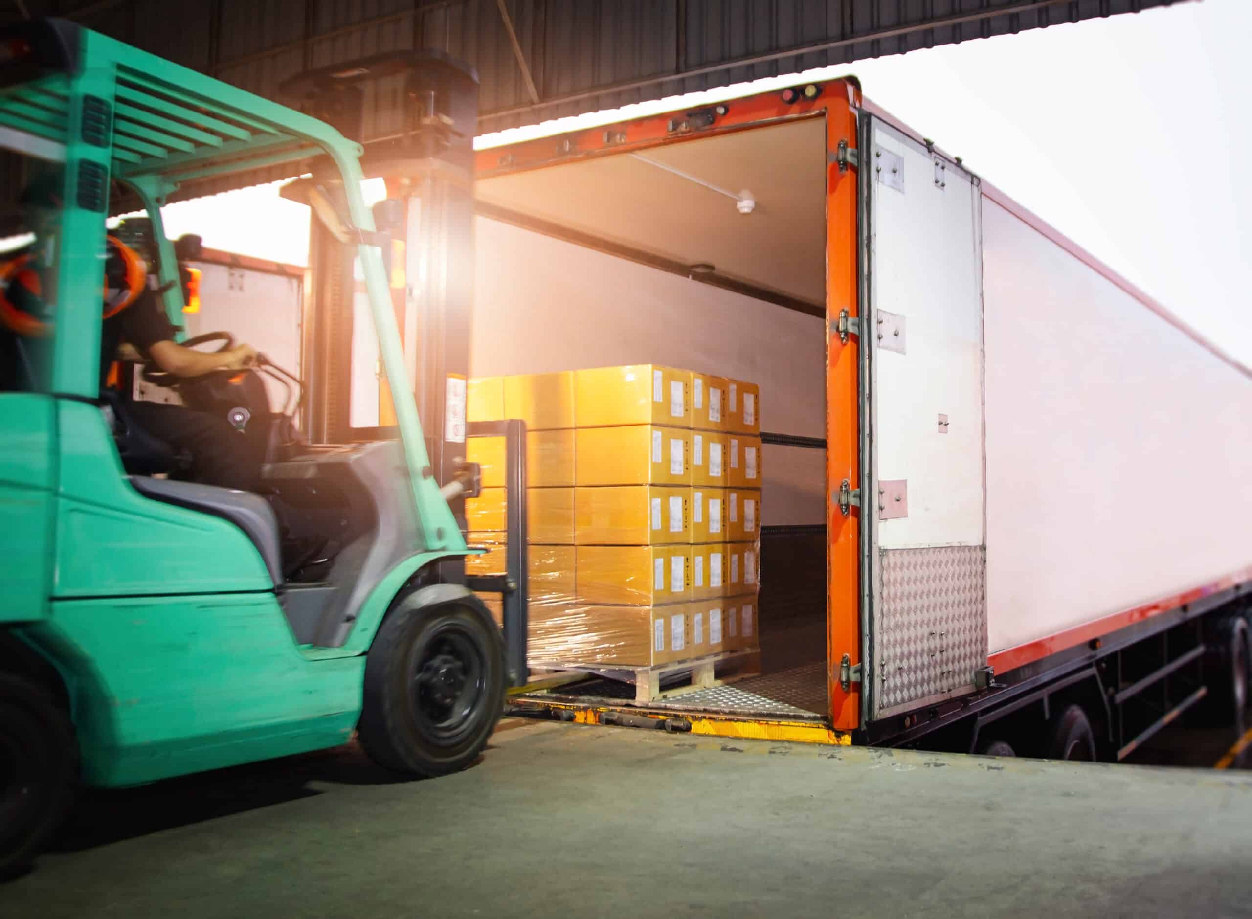 AdobeStock_420385610 Forklift lifting merchandise in a container.