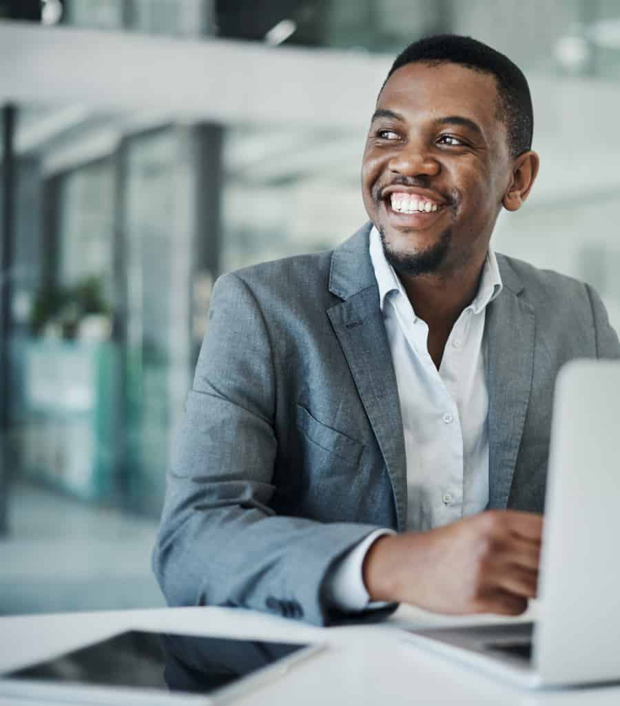 pharma-hero A smiling executive wearing a suit and using a laptop.