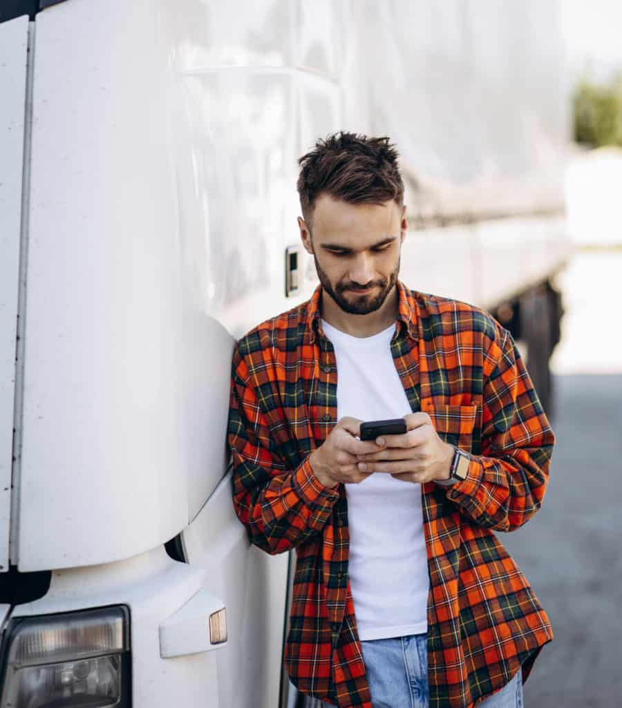 blog Person leaning on a truck while using his phone.