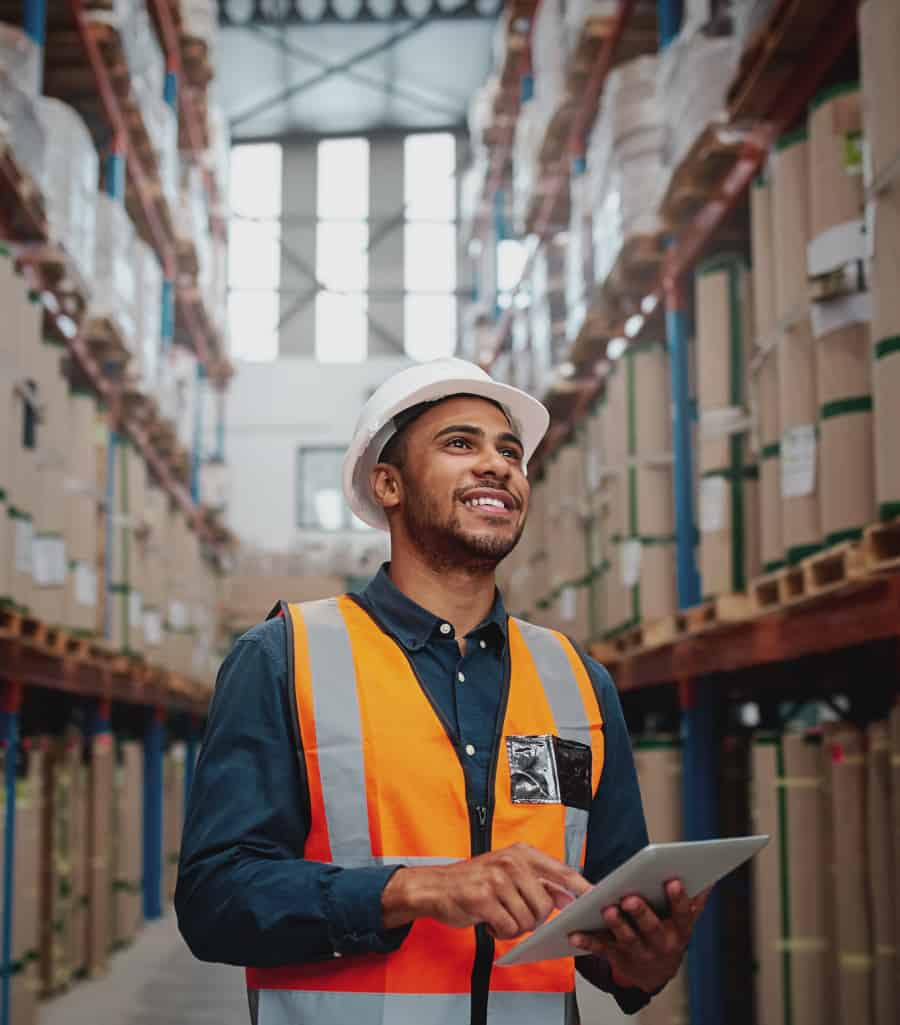Warehouse worker looking up at stocked shelves with a clipboard in hand.