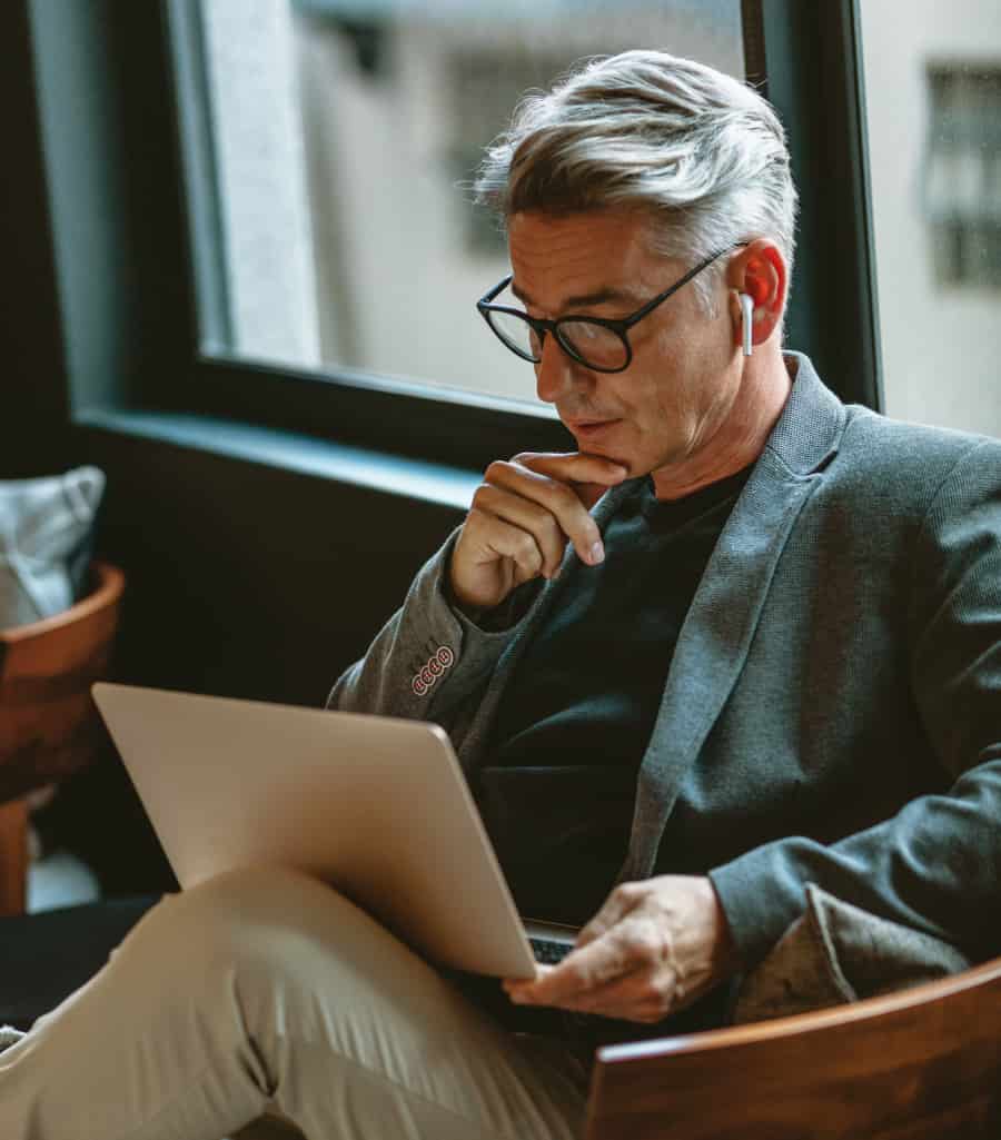 white-papers Man sitting on a piece of furniture using a laptop.