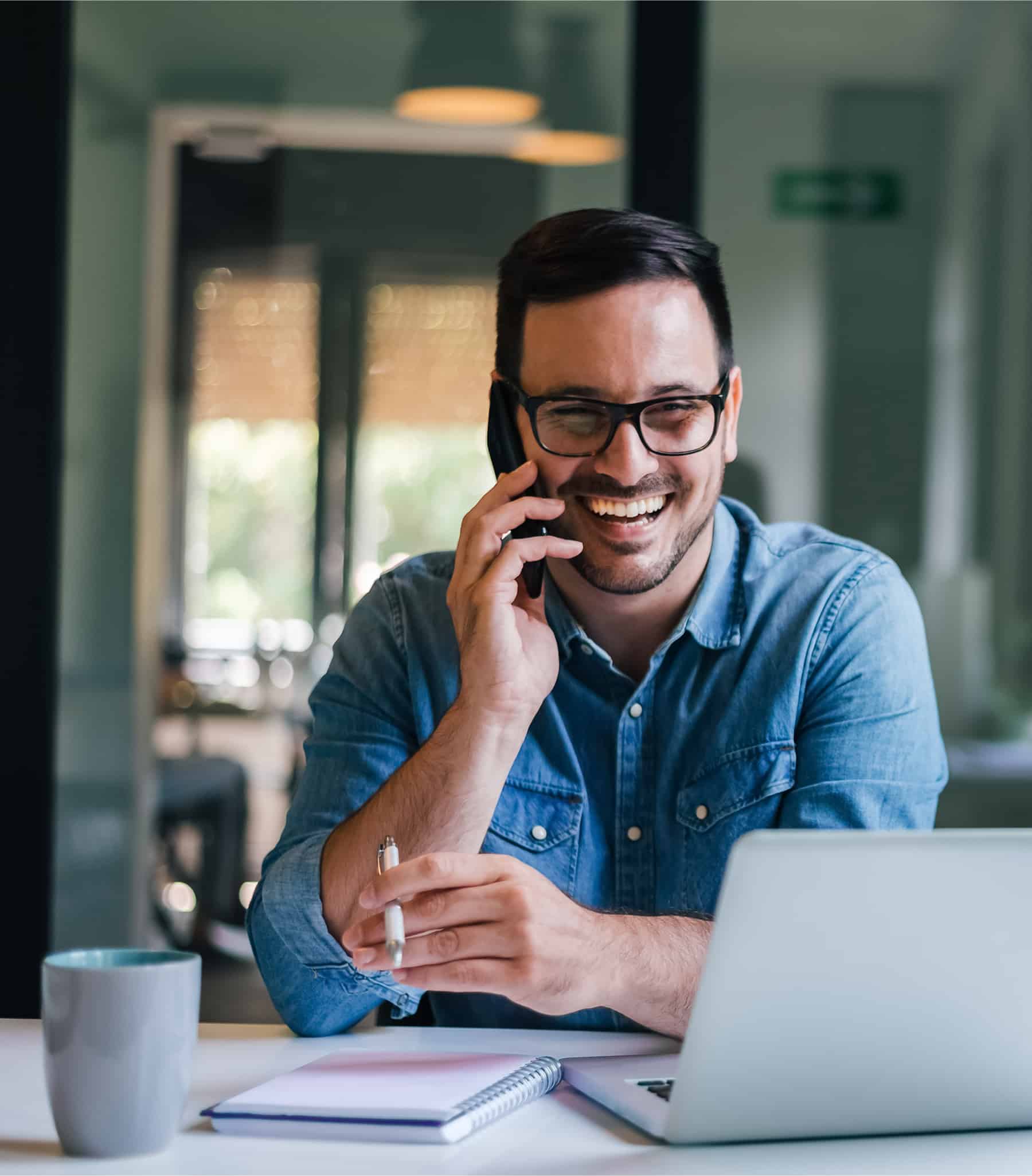 Smiling worker while talking on the phone and looking at his computer screen.