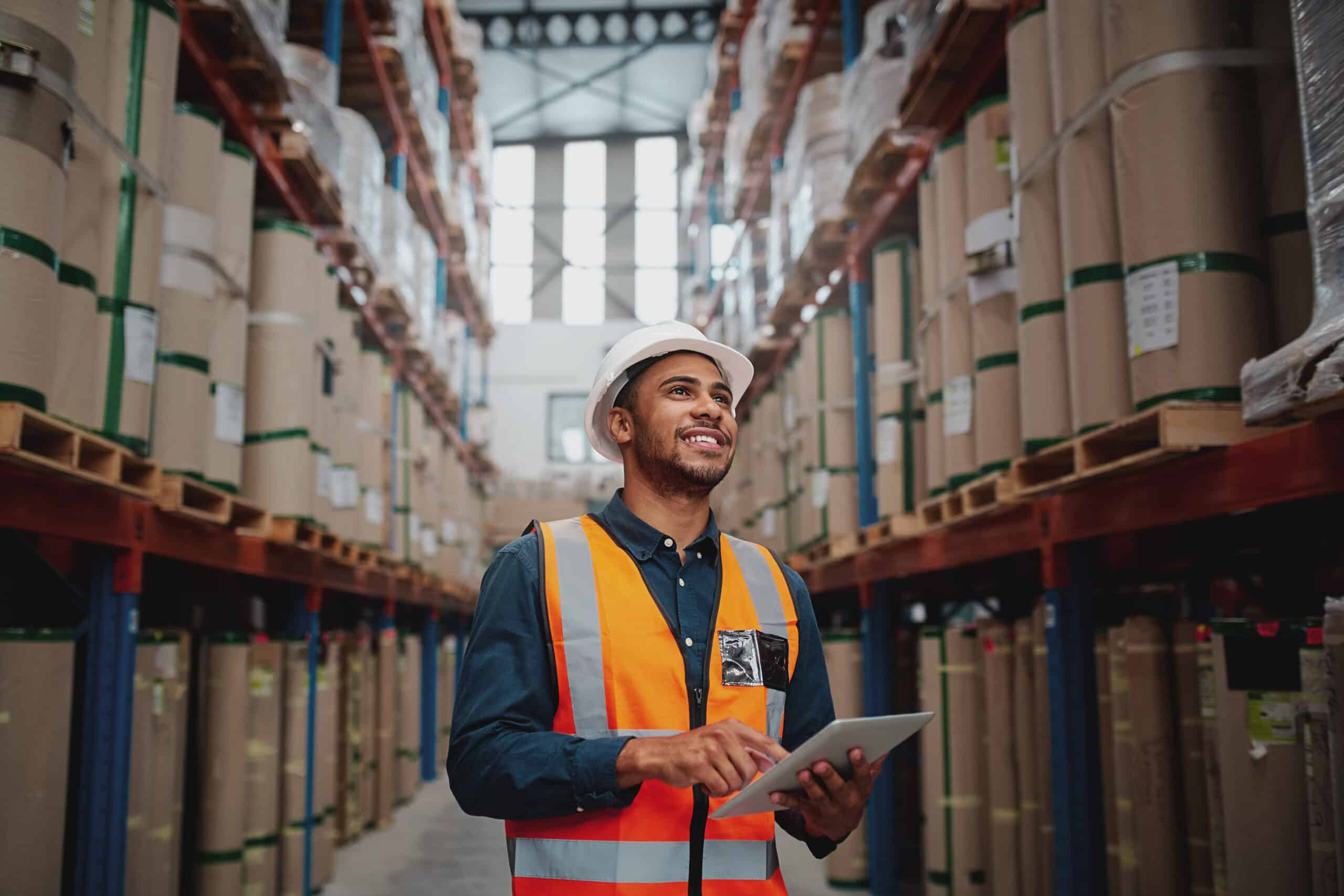 Low angle view of young african man wearing reflective jacket holding digital tablet standing in factory warehouse smiling Stanion Wholesale Electric.