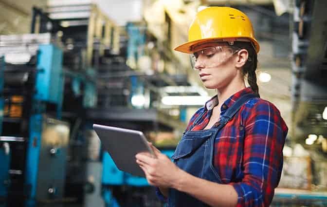 Manufacturing worker in a hard hat reviewing product data on a tablet
