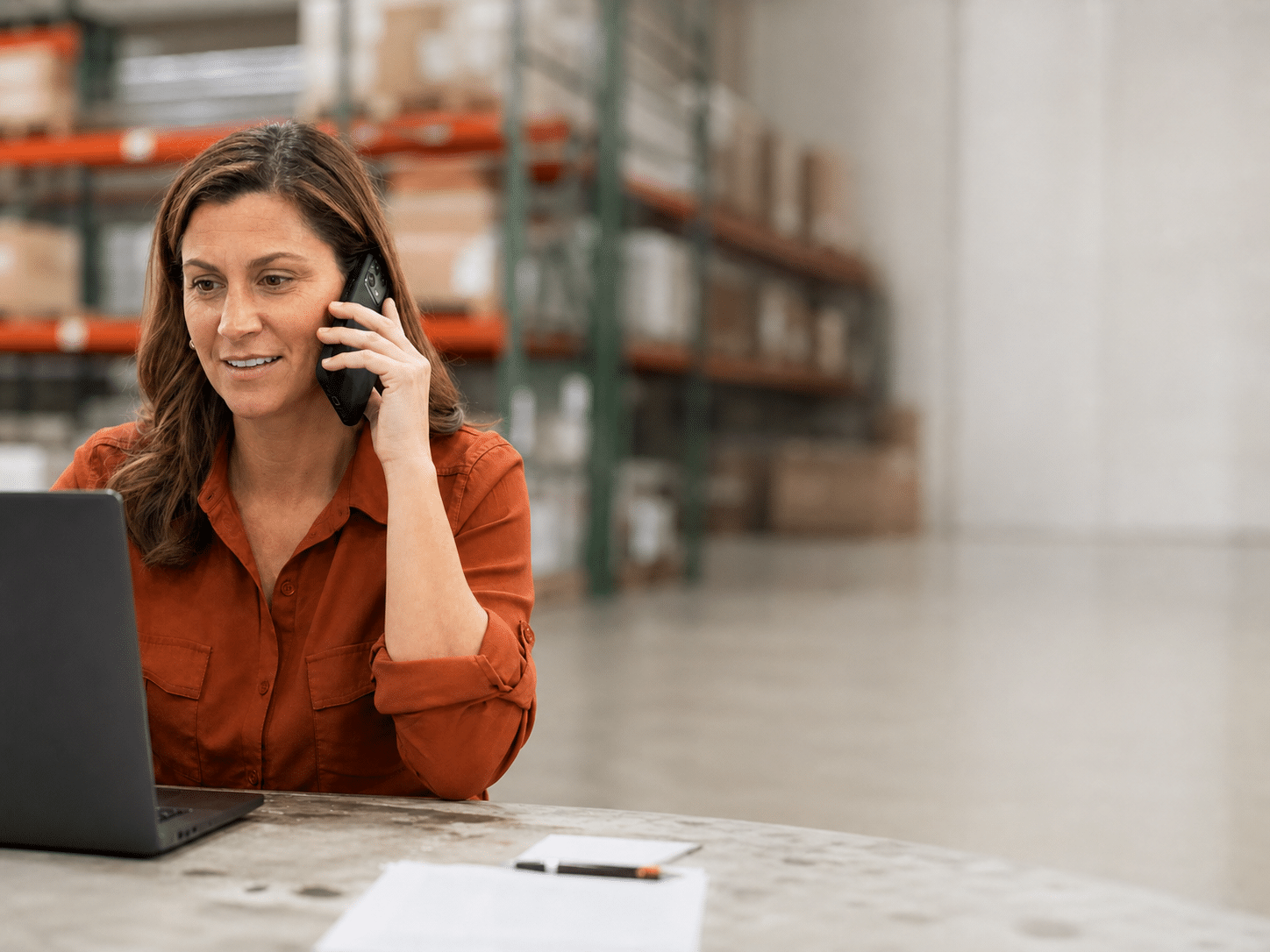 Distribution operations professional using a laptop and phone in a warehouse