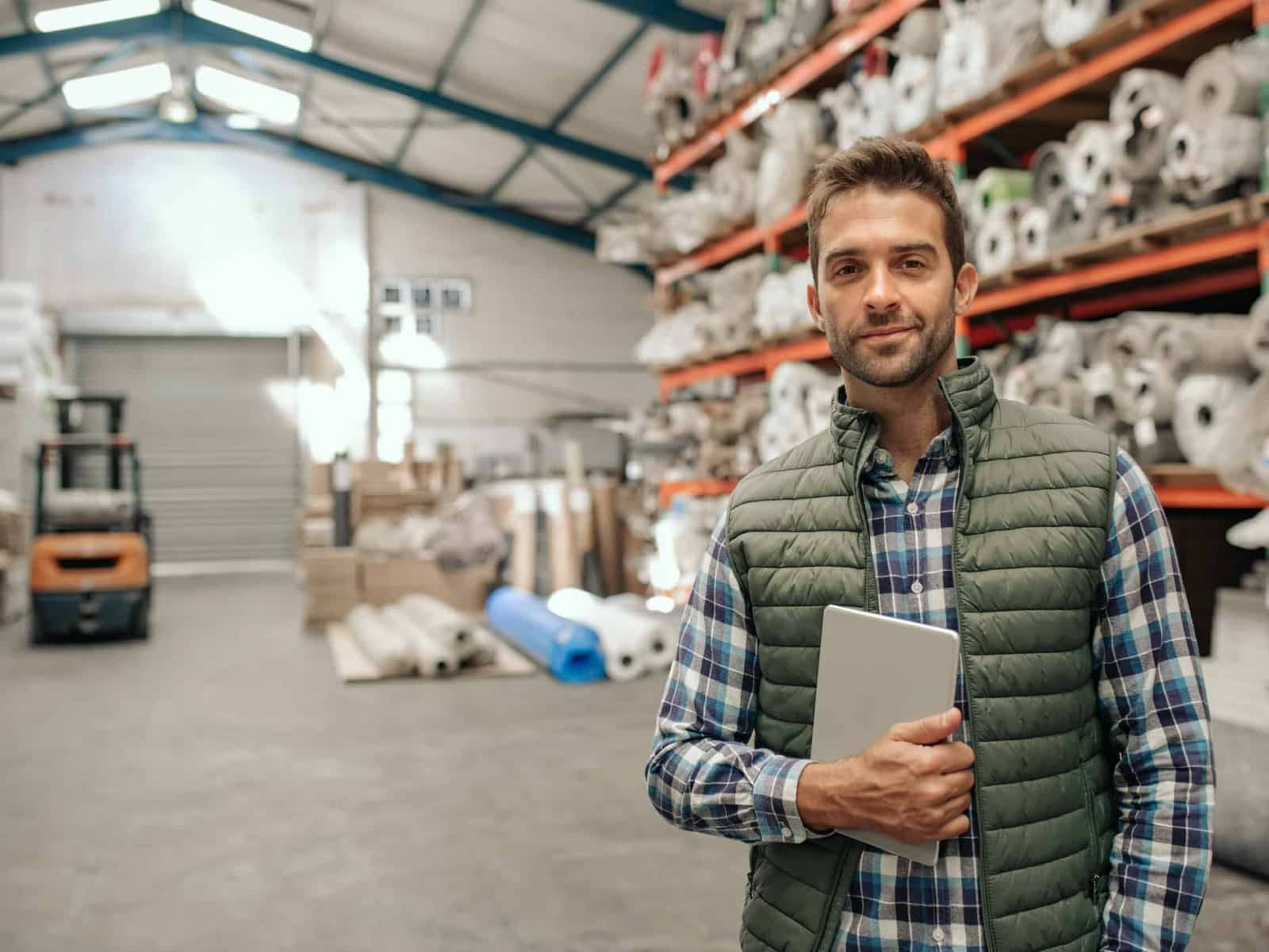 Industrial supply associate with a tablet in a stocked warehouse aisle
